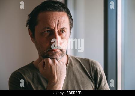 Ernstes kaukasisches reifes männliches Denken am Fenster der Wohnung, selektiver Fokus Stockfoto