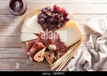 Wurstplatte mit Käse, Trauben und Figuren auf Holztisch Stockfoto