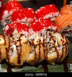 Nahaufnahme verschiedener Sushi-Brötchen mit knusprigem Tempura, Tobiko und frischem Lachs, aufgenommen in natürlicher Beleuchtung auf dunklem Hintergrund Stockfoto