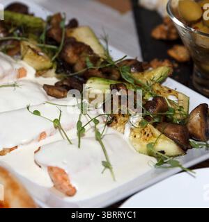 Gegrillte Lachsfilets mit weißer cremiger Sauce und Kräutern, serviert mit geröstetem Gemüse auf einem weißen Keramiktablett, Gourmet-Konzept Stockfoto