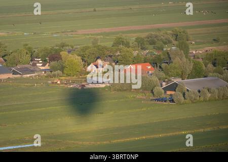 Schatten des Heißluftballons über flachem ländlichem Bauernhof in den Niederlanden. Grüne landwirtschaftlich genutzte Polderfelder in den Niederlanden Stockfoto