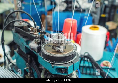 Textilindustrie, automatisches Stricken von Socken. Kreisförmige Strickmaschine auf verschwommenem Hintergrund von farbigen Fäden auf Spulen Stockfoto
