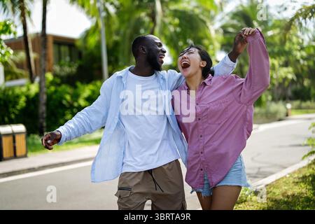 Glückliches, interrassisches Paar lacht zusammen draußen, genießt einen unbeschwerten Moment der Liebe, Freude Stockfoto