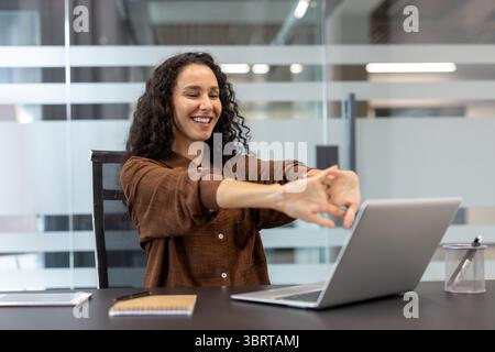 Eine lächelnde Frau dehnt sich an ihrem Schreibtisch aus und macht eine Pause von der Arbeit. Büroarbeitsplatz. Stockfoto