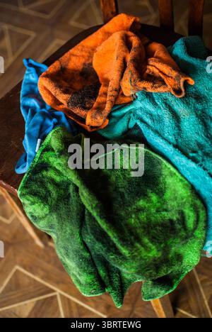 Ein Haufen bunter, schmutziger Lappen, die in der Nähe des Zerkleinerers auf dem Holzstuhl liegen. Alte Garage Stockfoto