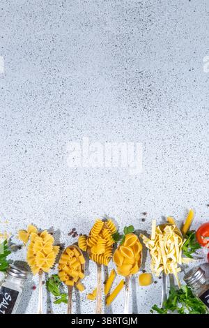 Verschiedene getrocknete Spaghetti, Nudeln, Pasta in Löffeln auf weißem Tischhintergrund. Verschiedene Formen Arten rohe italienische Pasta mit Kräutern, Olivenöl, tom Stockfoto