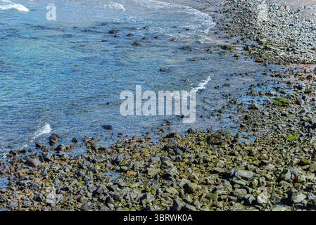 Blick auf die Strandwellen, die bei Ebbe auf dunklen Felsen brechen. Paradiesischer Strand. Tadellose Natur. Brasilien. Stockfoto