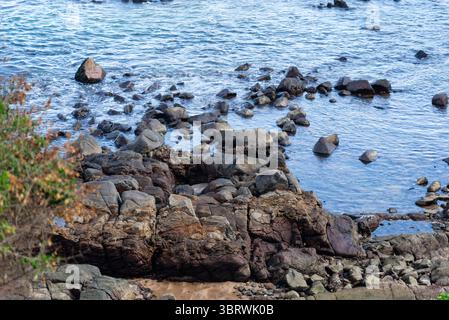 Blick auf die Strandwellen, die bei Ebbe auf dunklen Felsen brechen. Paradiesischer Strand. Tadellose Natur. Brasilien. Stockfoto