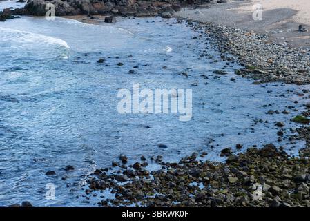 Blick auf die Strandwellen, die bei Ebbe auf dunklen Felsen brechen. Paradiesischer Strand. Tadellose Natur. Brasilien. Stockfoto