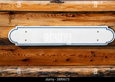 Ein leeres weißes Schild mit einem dünnen blauen Rand, das an einer Wand aus alten lackierten Holzdielen montiert ist und ein ideales Modell für Ihren Text oder Ihr Logo darstellt. Stockfoto
