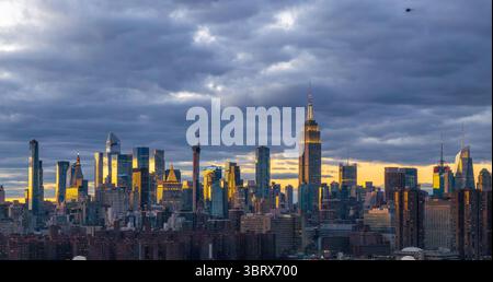 Aus der Vogelperspektive des Empire State Building inmitten einer goldenen Stadtlandschaft unter einem dramatischen Himmel, New York, USA. Stockfoto