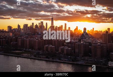 Aus der Vogelperspektive auf die Sonne, die unter dem Horizont eintaucht und einen goldenen Glanz auf die Wolkenkratzer von Manhattan wirft, einschließlich des One World Trade Center, New York, New York, USA. Stockfoto