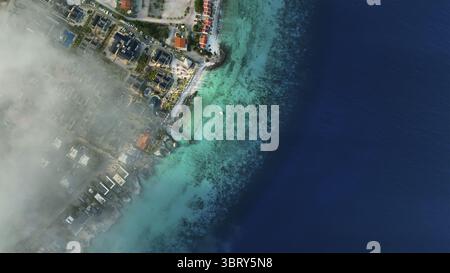 Aus der Vogelperspektive auf türkisfarbenes Wasser, das auf den dunkleren Ozean trifft, ein kleines Boot, das in der Nähe der Küste segelt, Kralendijk, Bonaire, Karibik Niederlande. Stockfoto