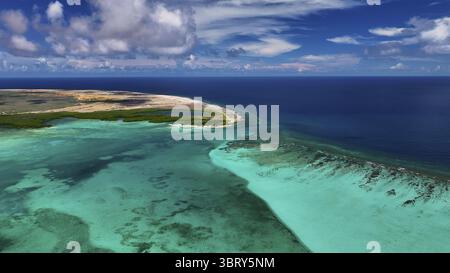 Aus der Vogelperspektive auf türkisfarbenes Wasser trifft auf die Sandküste einer Insel mit verstreutem Grün unter einem lebendigen Himmel, Kralendijk, Bonaire, Karibik Niederlande. Stockfoto