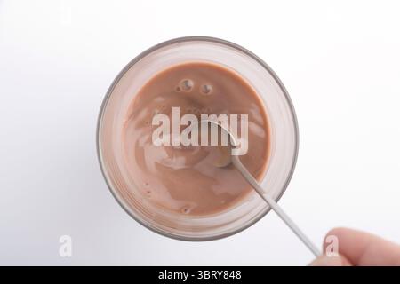 Zubereitung von Kakaogetränk im Glas, Hinzufügen von Milch zu Kokaenergie von oben auf weißem Hintergrund Stockfoto