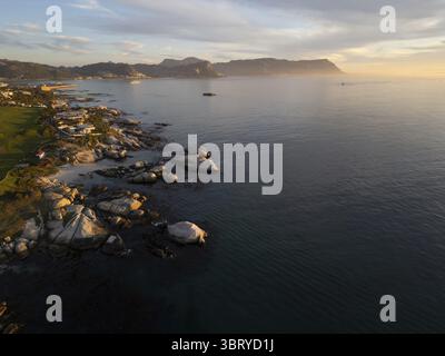 Der Blick auf die zerklüftete Küste trifft auf das ruhige Meer in der Nähe von Llandudno Beach, während die Berge mit dem goldenen Licht der Sonne in den Horizont eintauchen, Kapstadt, Westkap, Südafrika. Stockfoto