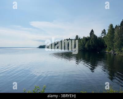 Der ruhige See spiegelt den üppig grünen Wald unter einem hellblauen Himmel wider. Stockfoto