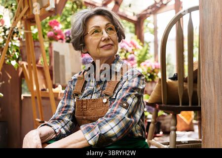 Eine ruhige Seniorin genießt die Natur, umgeben von lebendigen Blumen und Grün. Stockfoto