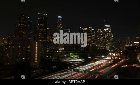 Los Angeles, USA - 25. Juni 2025: Aus der Vogelperspektive eine pulsierende Skyline der Stadt mit goldenen Lichtern, die von den unscharfen Pfaden vorbeifahrender Autos auf den Autobahnen durchzogen werden. Stockfoto