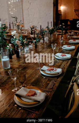 Ein wunderschön gestalteter rustikaler Hochzeitsempfangstisch mit floralen Mittelstücken, Kerzen und elegantem Speisesaal sorgt für eine warme und einladende Atmosphäre Stockfoto