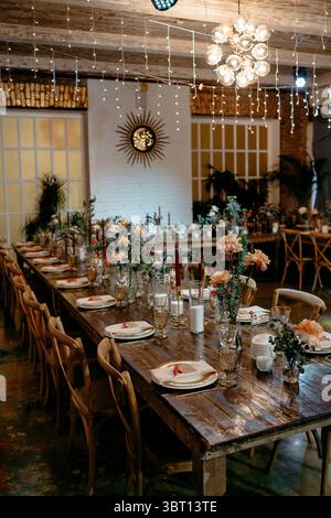 Ein rustikaler Hochzeitsempfang verfügt über einen wunderschön gestalteten langen Tisch mit Blumendekor, Holzstühlen, Kerzenlicht und ein warmes, elegantes Ambiente. Stockfoto
