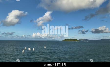 Aus der Vogelperspektive tanzen weiße Segel über dem tiefblauen Meer und spiegeln die flauschigen Wolken über der grünen Insel Santa Catarina, Kalifornien, USA. Stockfoto