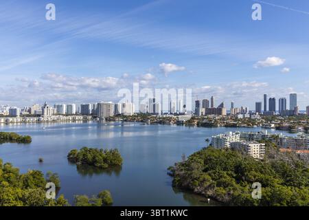 Aus der Vogelperspektive auf eine atemberaubende Stadtlandschaft, die sich im ruhigen Wasser in der Nähe von üppig grünen Inseln und Gebäuden spiegelt, Aventura, Florida, USA. Stockfoto