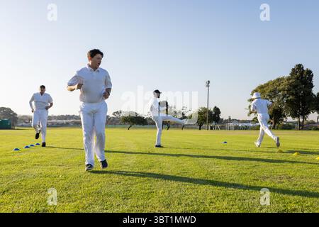 Männliche Mannschaftskameraden in weißen Uniformen, die mit einem Fanghandschuh durch Kegelbahnen auf dem Sportplatz laufen Stockfoto