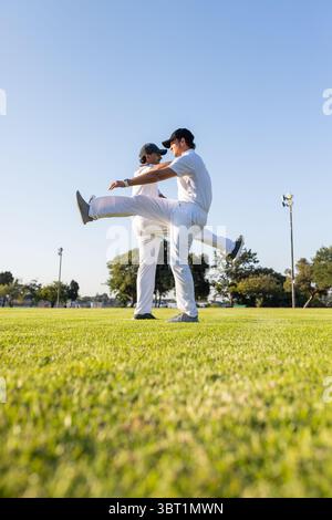 Verschiedene männliche Mannschaftskameraden dehnen sich in weißen Uniformen auf dem Gras nach vorne Stockfoto