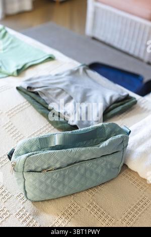 Hellblauer gesteppter Kulturbeutel auf beigefarbener Strickdecke in der Nähe eines offenen dunkelblauen Koffers Stockfoto