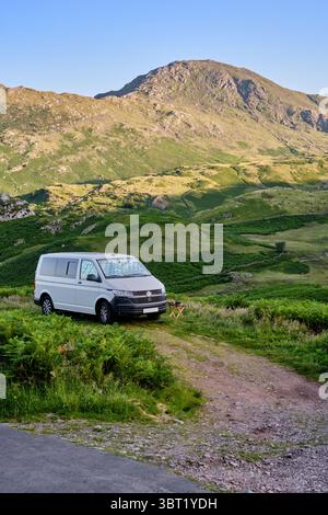 Ein VW Transporter Wohnmobil parkte über Nacht bei Blea Moss im Lake District National Park mit dem Wetherlam Peak in der Ferne an einem sonnigen Abend. Stockfoto