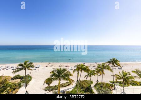 Blick aus der Vogelperspektive auf einen strahlenden Strand mit Palmen, türkisfarbenem Wasser und Sonnenanbetern, die sich im Sonnenschein sonnen, Miami Beach, Florida, USA. Stockfoto