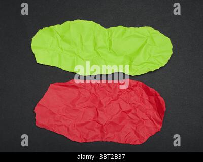 Zwei unregelmäßig geformte Stücke zerknitterten Papiers, eines rot und eines grün, auf dunklem Hintergrund. Stockfoto