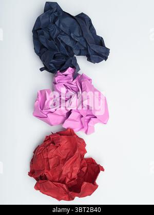Drei zerknitterte Papierstücke in verschiedenen Farben: Dunkelblau, Hellrosa und Rot. Stockfoto