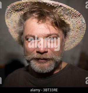 Ein Mann mit Gesichtsbehaarung mit Strohhut und gepflegtem Bart, der seine definierte Kiefer betont. Er verströmt Charme und Stil mit seiner Auswahl an Kopfbedeckungen Stockfoto