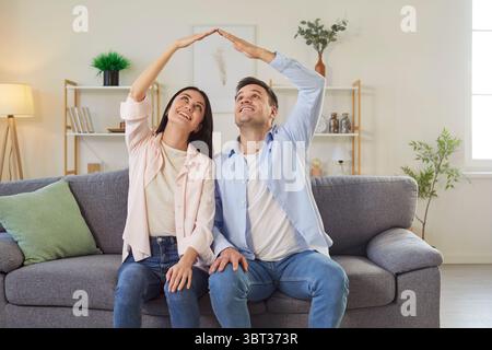 Familienpaar Zeigt Das Dachschild Auf Dem Sofa Zu Hause Stockfoto