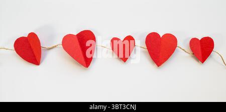 Eine Kette von Herzen mit einem leeren Papier, Herzen hängen an einer Schnur, leere Stelle für Nachrichten, flach zum Valentinstag, kreativer rosafarbener Hintergrund weiß Stockfoto
