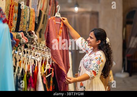 Die junge asiatische Frau, die in Mumbai auf der Fashion Street shoppt, sieht sich wunderschöne Kleider im Kaftan-Stil an Stockfoto