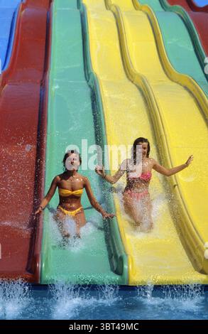Zwei junge Frauen mit blonden Haaren gleiten in den Sommerferien am Pool auf der Rodelbahn Stockfoto