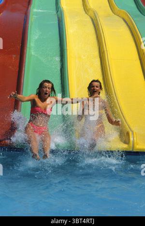 Zwei junge Frauen mit blonden Haaren gleiten in den Sommerferien am Pool auf der Rodelbahn Stockfoto