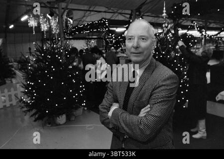 Dekoration eines Weihnachtsbaums durch die Bürgermeisterin der Region und Porträt von Mr. Kooy aus dem Gartencenter Christmas and Christmas Trees Gardens and Parks, Whizgle News, Dutch Desk, Niederlande, 1950 - 2000 am 09-12-1985. Diese Themen werden in der Abbildung angezeigt. Die Szene fängt ein lebhaftes Innenleben ein, das offensichtlich für einen festlichen Anlass geschmückt ist, wahrscheinlich um Weihnachten herum. Im Vordergrund steht eine gut gekleidete Person selbstbewusst mit gekreuzten Armen und strahlt ein Gefühl von Stolz oder Nachsicht aus. Die Kleidung ist klassisch und mit einem karierten Blazer, der einen Hauch von Eleganz verleiht Stockfoto