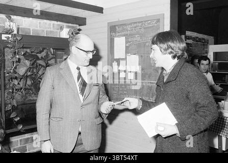 Jubiläumsaquarium ver. IJm. Jubiläumsjubiläen, Whizgle News, Dutch Desk, Niederlande, 1950 - 2000 am 03-02-1978. Das Bild enthält diese Themen. In einem gemütlichen Innenbereich sind zwei Figuren in einem Moment des Austausches beteiligt. Die erste Person, die wie ein älterer Mann aussieht, trägt einen scharfen, dunklen Anzug mit einer gestreiften Krawatte, die einen Hauch von Formalität verleiht. Er steht selbstbewusst und blickt direkt auf die jüngere Figur vor ihm. Seine Haare sind sauber gekämmt und er wirkt freundlich und doch professionell. Der jüngere Mann, der einen dunklen, strukturierten Mantel trägt, der Wärme und Möglichkeiten suggeriert Stockfoto