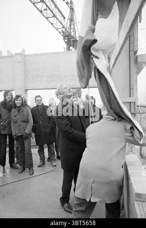 Eröffnung der Lorentz School Community Eröffnungen Inbetriebnahme, Whizgle News, Dutch Desk, Niederlande, 1950 - 2000 am 18.02.1972. Das Bild enthält diese Themen. In einer monochromatischen Szene steht eine Gruppe von Individuen in der Nähe einer Baustelle. Die Stimmung scheint eine von Vorfreude und Feiern zu sein. Im Vordergrund wird ein Mann in einem langen, dunklen Mantel mit der Enthüllung beschäftigt, indem er eine große Fahne oder ein Banner herunterzieht, die über einem strukturellen Element hängen. Sein Ausdruck deutet auf einen Moment des Stolzes oder der Bedeutung hin. Um ihn herum beobachten mehrere Leute das Ereignis. Ihre unterschiedliche Haltung Stockfoto