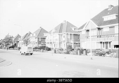 Houses Heemskerk Buildings, Whizgle News, Dutch Desk, Niederlande, 1950 - 2000 am 24-05-1965. Dies sind die Themen im Bild. Die Szene zeigt eine Vorstadtstraße, gesäumt von Wohnhäusern, die jeweils charakteristische architektonische Merkmale aufweisen. Die Häuser, überwiegend zweistöckig, weisen eine Mischung aus Ziegelsteinen und strukturierten Fassaden auf, durchsetzt von Giebeldächern, die mit roten Fliesen verziert sind. Die gesamte Farbpalette neigt zu gedämpften Grau- und Weißtönen und verleiht der Szene ein fast monochromatisches Gefühl. Im Vordergrund verläuft eine schmale Straße parallel zur Häuserlinie, in der ein einfacher Van geparkt ist Stockfoto