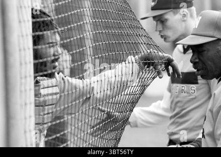 Baseball Nieuw-Vennep - VUC, Whizgle News, Dutch Desk, Niederlande, 1950 - 2000 am 27-04-1991. Dies sind die Elemente im Bild. In einer dynamischen Szene interagieren drei Individuen in der Nähe eines Maschendrahtzaugs, der als Brennpunkt der Komposition dient. Das Ambiente spiegelt eine Mischung aus Intensität und Kontemplation wider. Links lehnt sich ein junger Mann mit zerzausten Haaren an den Zaun, sein Ausdruck zeigt eine Mischung aus Entschlossenheit und Besorgnis. Er trägt ein helles Trikot, das einen starken Kontrast zu den dunklen, strukturierten Haarsträhnen bildet. Sein Blick ist auf die rechte Seite des f gerichtet Stockfoto