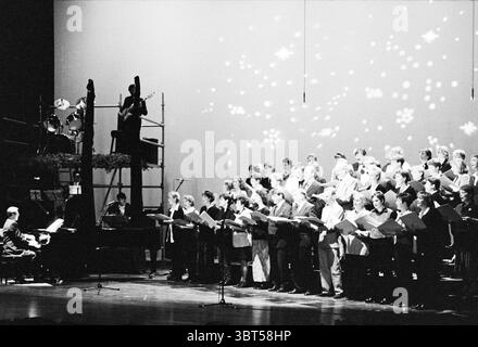 Chor Odyssey in the Meerse Hoofddorp Hoofddorp Raadhuisplein the Netherlands, Whizgle News, Dutch Desk, Niederlande, 1950 - 2000 am 19.12.1997. Diese Themen werden in der Abbildung angezeigt. In einem schwach beleuchteten Aufführungsraum steht ein großer Chor in einem Halbkreis, der in koordinierende Kleidung gekleidet ist, die wahrscheinlich verschiedene Schwarz-weiß-Farbtöne enthält. Ihre Ausdrucksformen reichen von fokussiert bis fröhlich, wenn sie sich mit der Musik beschäftigen. Einige halten Noten in der Hand, während andere mit Begeisterung kraftvolle, harmonische Noten liefern. Ein Flügel befindet sich etwas links, mit einem Mus Stockfoto