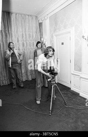 Pressekonferenz Rough Diamond Amsterdam (Ariola) Music, Whizgle News, Dutch Desk, Niederlande, 1950 - 2000 am 15-02-1977. Das Bild enthält diese Themen. Ein geräumiger Innenraum ist dargestellt, der sich durch seine sanfte, gedämpfte Farbpalette auszeichnet. Die Wände sind mit hellen Tapeten mit dezenten Mustern verziert, die eine warme und einladende Atmosphäre schaffen. Satte, schwere Vorhänge in einem ähnlichen Schatten wie der Wandvorhang, elegant neben einem Fenster, filtrieren weiches, diffuses Licht, das die gemütliche Stimmung der Szene unterstreicht. Im Vordergrund steht ein junger Mensch mit fokussierter Absicht, Hocke Stockfoto
