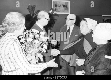 Installation von Bürgermeister Machielsen Zandvoort Mayors, Whizgle News, Dutch Desk, Niederlande, 1950 - 2000 am 05-10-1977. Dies sind die Themen im Bild. In einem warm beleuchteten Innenbereich findet eine Versammlung von mehreren Personen statt. Der Raum ist mit üppigen grünen Pflanzen im Hintergrund geschmückt, die eine natürliche und einladende Atmosphäre schaffen. Ein gerahmtes Kunstwerk mit Pferden ist an der Wand zu sehen und verleiht der Umgebung einen Hauch von Eleganz. Im Vordergrund sind zwei Männer in einem Handschlag verwickelt, der einen Moment der Begrüßung oder Feier andeutet. Ein Mann trägt Glas Stockfoto