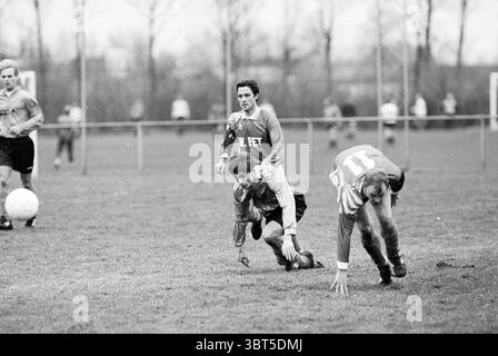 Football Sizo - SMS, Whizgle News, Dutch Desk, Niederlande, 1950 - 2000 am 22-01-1993. Diese Themen sind in der Abbildung dargestellt. Die Szene zeigt einen dynamischen Moment auf einem grasbewachsenen Feld, wahrscheinlich Teil eines Fußballspiels. Die Atmosphäre ist eindeutig energiegeladen, die Spieler sind aktiv und ein Gefühl von Wettkampf erfüllt die Luft. Im Vordergrund sind zwei Spieler an einem Wettbewerb beteiligt. Ein Spieler, der in einem grauen Trikot gekleidet ist, liegt vielleicht nach einem Sturz auf dem Boden, während ein anderer in einem knallroten Trikot scheint, als ob er auf den Ball zustürzt oder krabbelt. Das Gras darunter ist ein leuchtendes Grün, kontrastreich Stockfoto