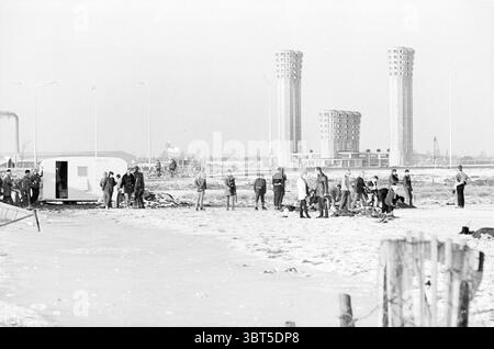 Skating-Spaß auf einem See in der Nähe des Velsertunnels, Whizgle News, Dutch Desk, Niederlande, 1950 - 2000 am 01-1966. Die Abbildung zeigt diese Themen. Die Szene zeigt eine krasse Winterlandschaft, die von einer Gruppe von Menschen dominiert wird, die verschiedene Aktivitäten entlang einer schneebedeckten Fläche ausüben. Eine kalte Atmosphäre durchdringt die Umgebung, gekennzeichnet durch gedämpfte Grau- und Weißtöne, die ein Gefühl von Stille und Verzweiflung hervorrufen. Im Vordergrund sind Individuen über den verschneiten Boden verstreut, einige sind in kleinen Gruppen versammelt, während andere scheinbar unabhängig arbeiten. Sie sind im schweren Winter gekleidet Stockfoto